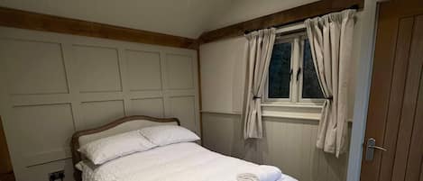A bedroom with a bed, a window with curtains, a door, and a wooden floor.