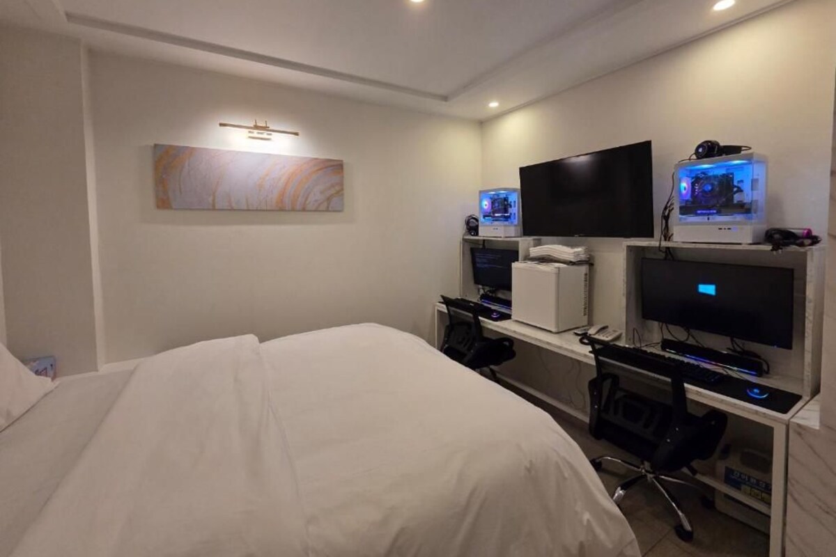 A hotel room with a bed, a desk with a computer setup, a flat-screen TV, and a wall-mounted artwork.