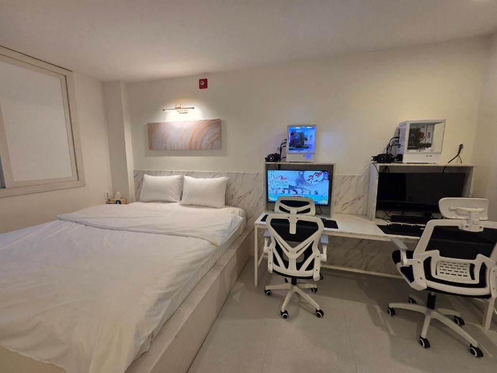 A hotel room with a bed, a desk with a computer, a chair, and a television.