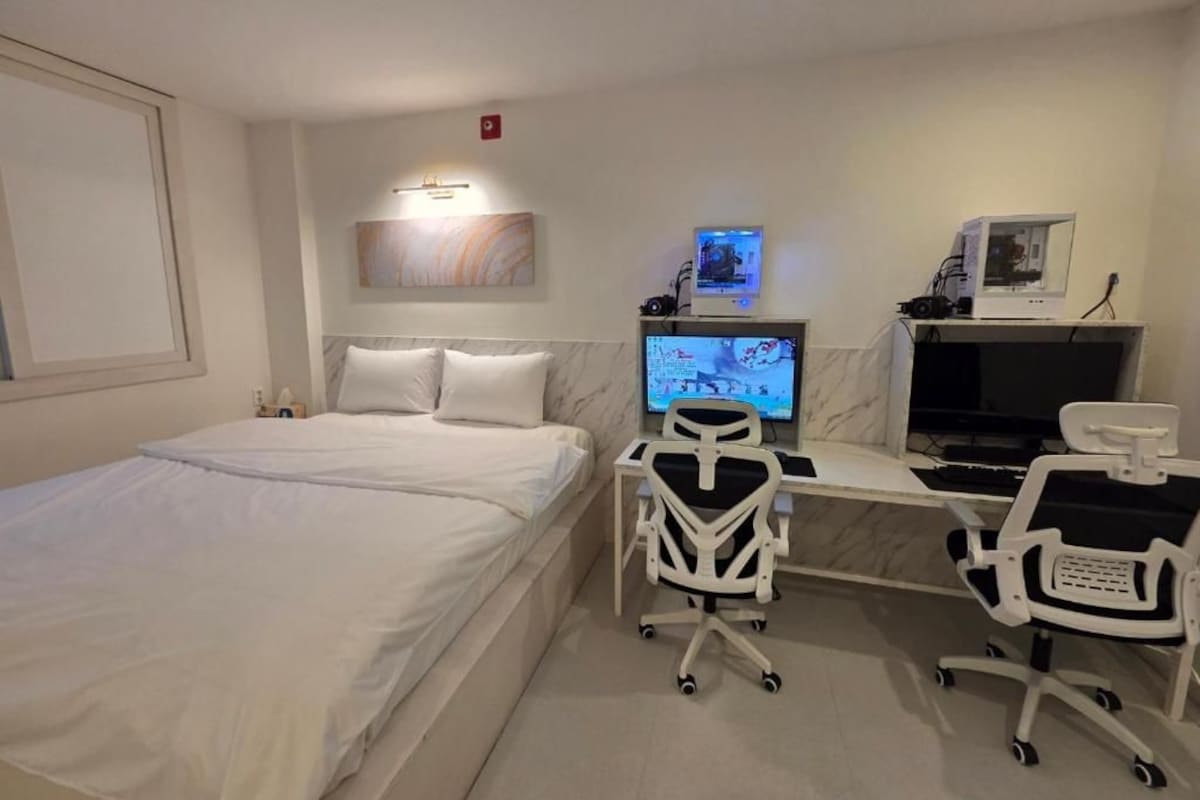 A hotel room with a bed, a desk with a computer, a chair, and a television.