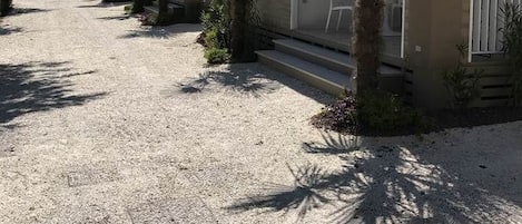 A row of single-story buildings with a gravel driveway, palm trees, and a clear blue sky.
