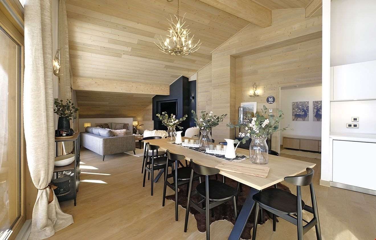 Un comedor moderno con una mesa de madera, sillas negras y una araña.