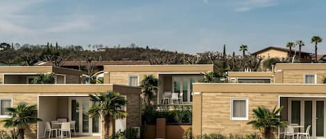 A modern resort with multiple units featuring balconies, outdoor seating, and a view of a hilly landscape.