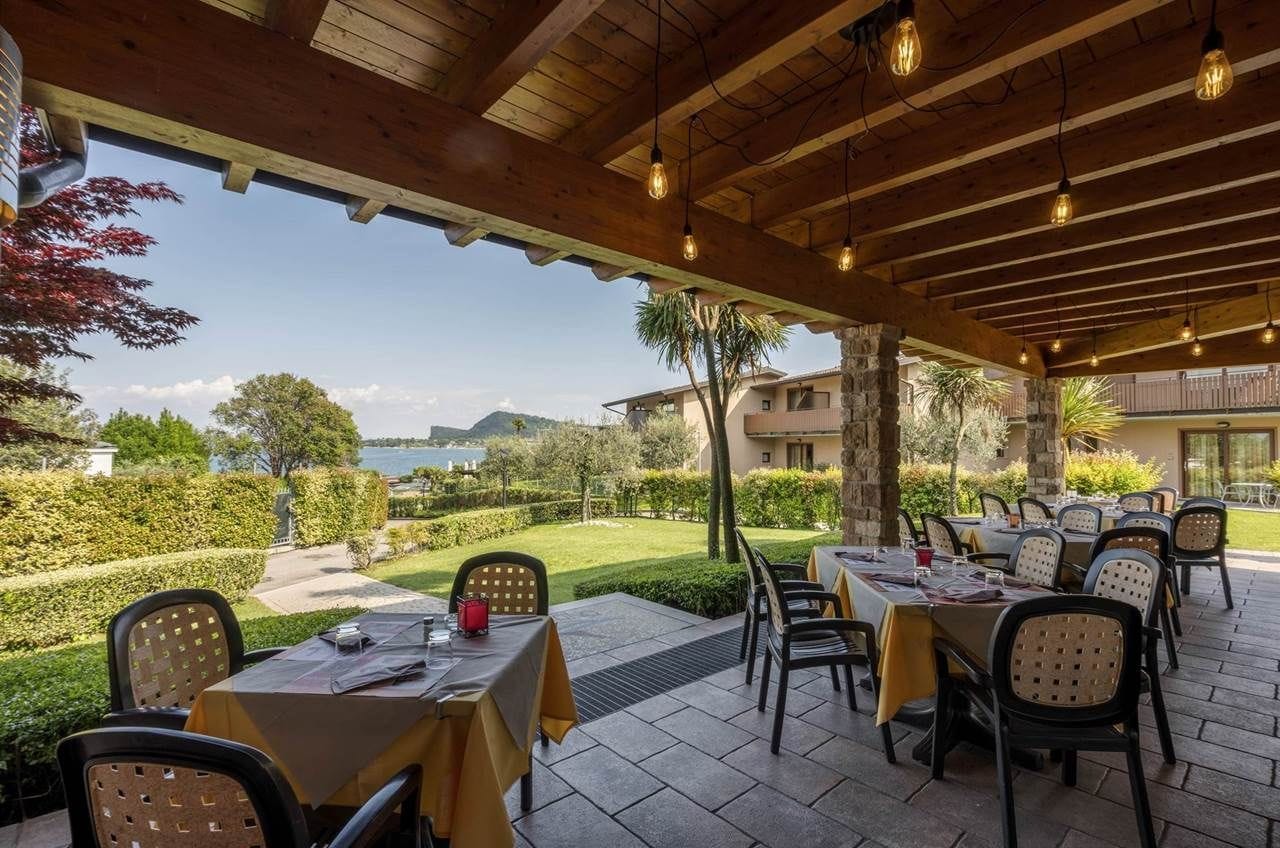 An outdoor dining area with tables and chairs, a view of the sea, and a stone building in the background.