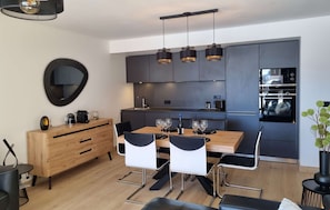 A modern kitchen with a dining area, featuring a wooden table, black chairs, and a built-in oven. - R Sidence Phoenix B13 3p6p (Huez)