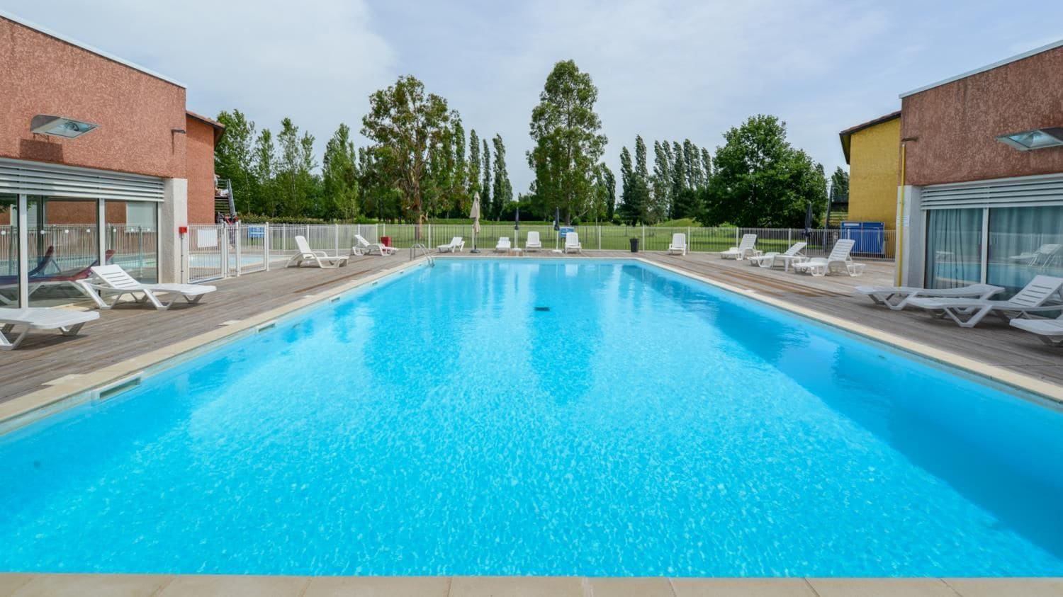 Una piscina rectangular amb aigua blava cristal·lina, envoltada de gandules blanques i un pont de fusta.