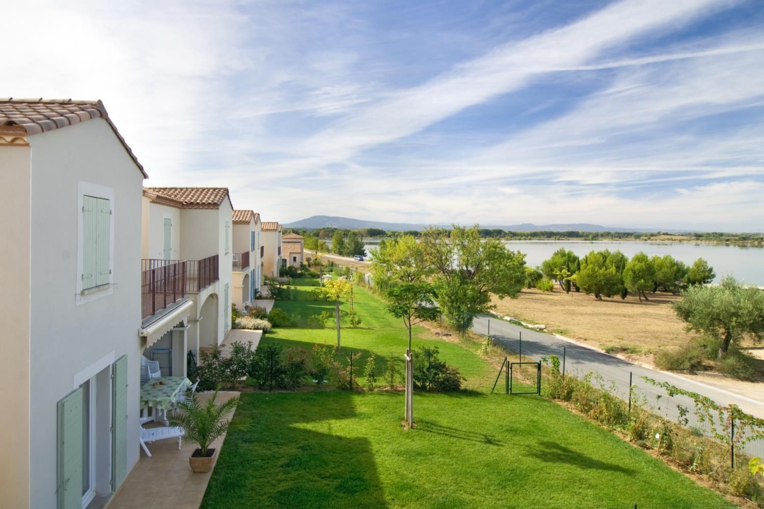 A residential building with a balcony, a well-maintained lawn, and a view of a lake.