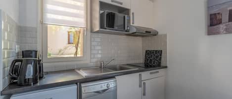 A compact kitchen with a dishwasher, a coffee maker, a microwave, and a window with blinds.