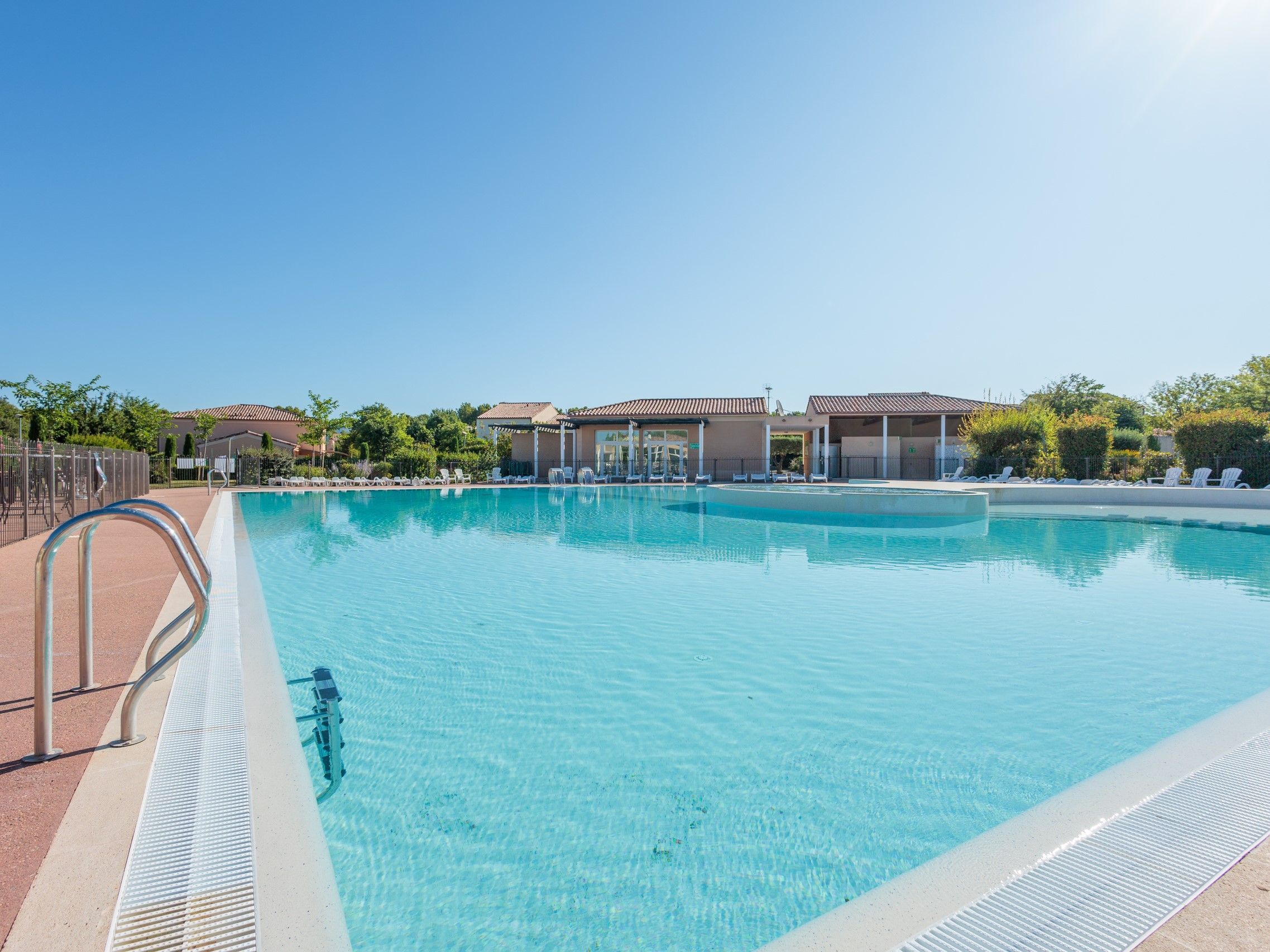 Une piscine d’un bleu éclatant, avec un escalier en métal sur le côté gauche, entourée de chaises longues et d’un espace abrité sous un toit.