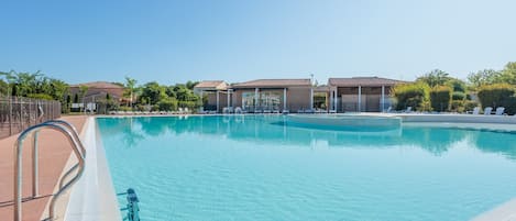 Une piscine d’un bleu éclatant, avec un escalier en métal sur le côté gauche, entourée de chaises longues et d’un espace abrité sous un toit.