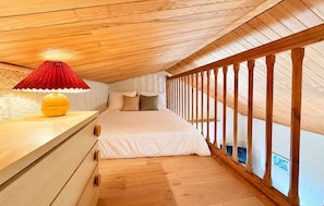 Un dormitorio con techo de madera, cama con ropa blanca, lámpara roja y barandal de madera.