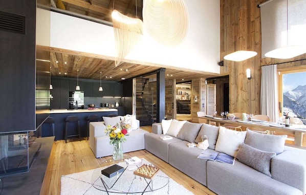A modern living room with a sofa, a coffee table, and a dining area with a table and chairs. - Chalet des 3 Ours 11p 3 Levels (Les Deux Alpes)