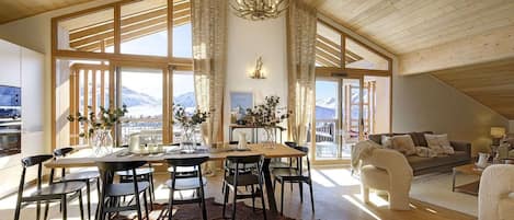 A spacious living area with a high ceiling, large windows, and a view of the mountains.