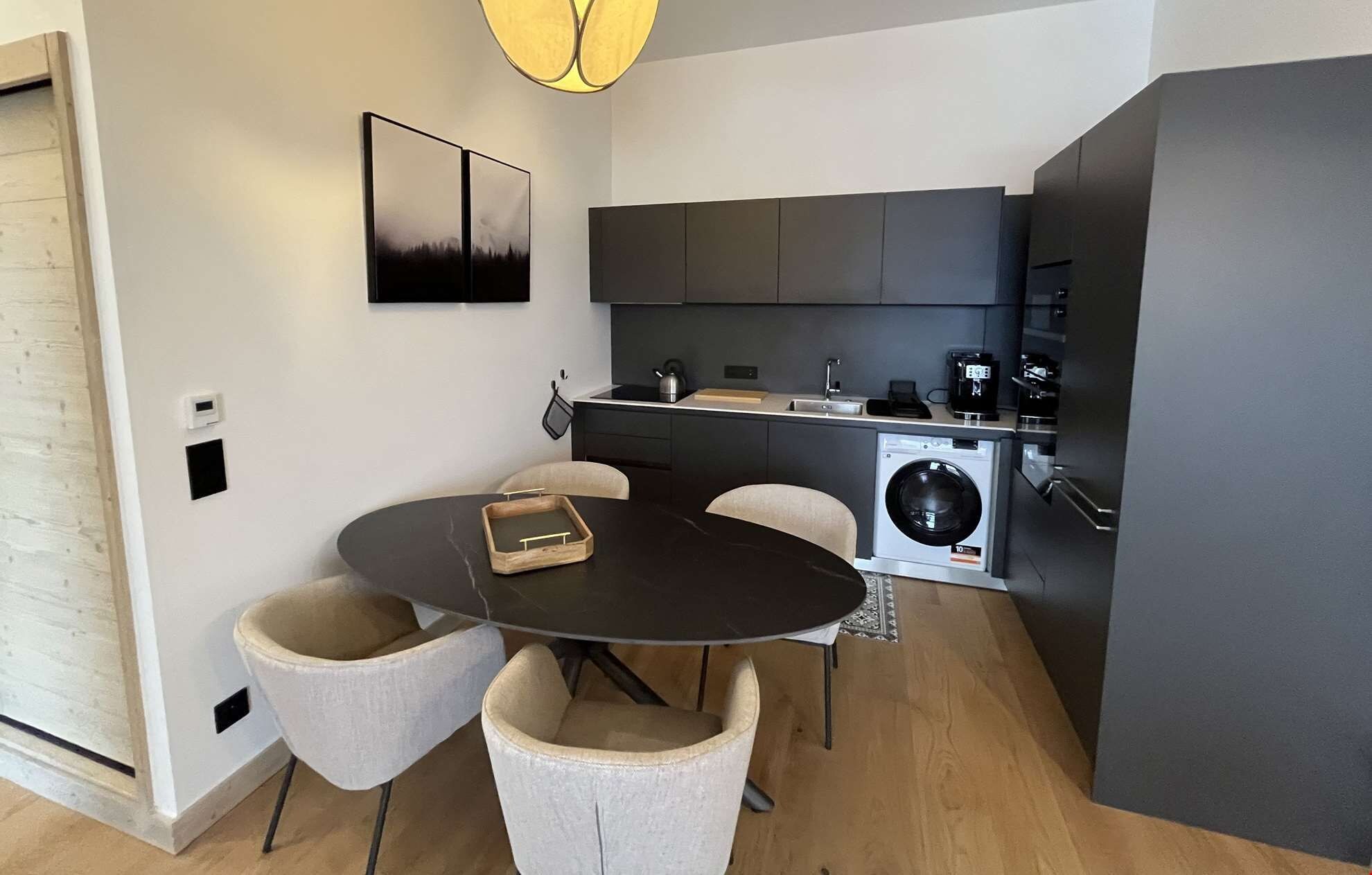A compact kitchen with a built-in washing machine, a dining table with chairs, and a modern pendant light.