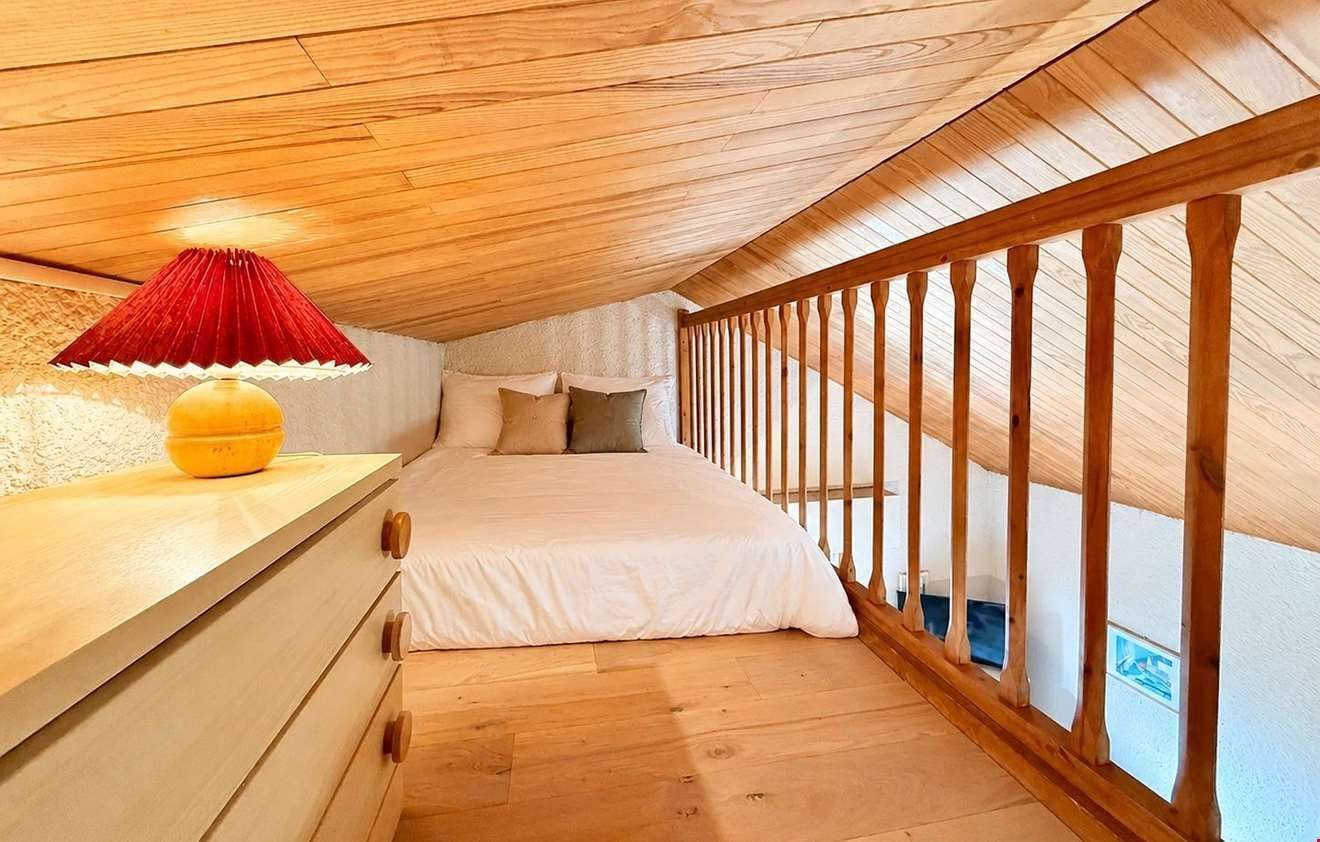 A bedroom with a wooden ceiling, a bed with white bedding, a red lamp, and a wooden railing.
