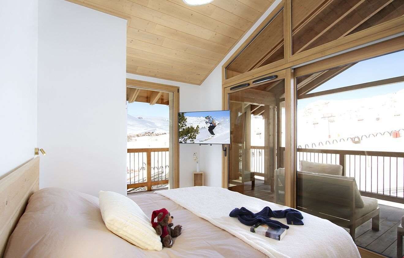 Un dormitorio con cama, televisión y balcón con vista a un paisaje nevado.