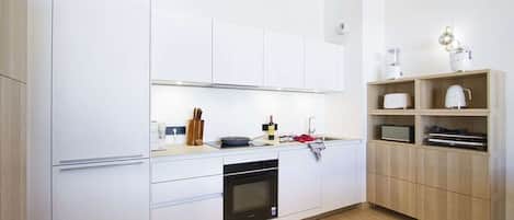 A modern kitchen with white cabinetry, a built-in oven, and a wooden shelf unit.