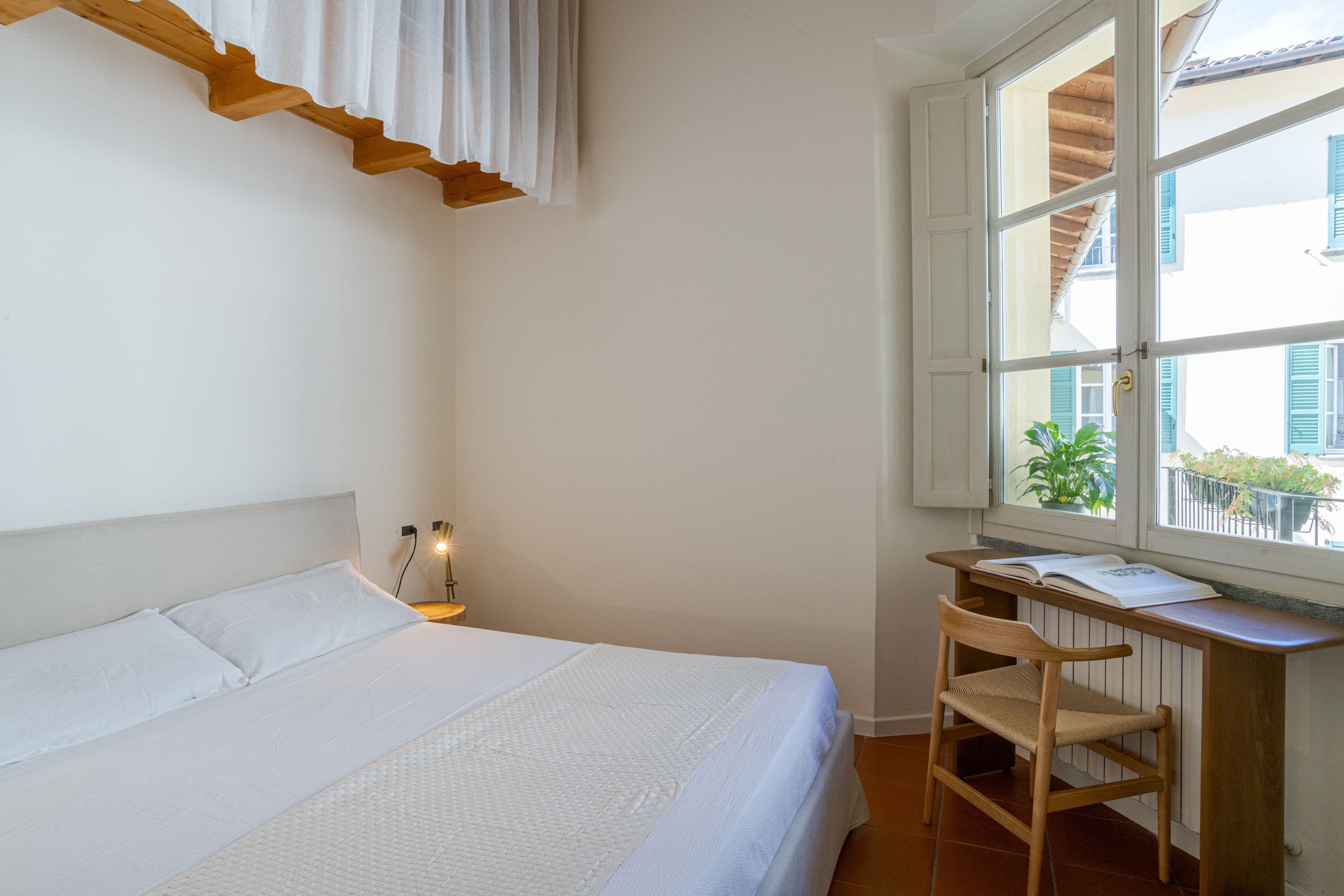 A bedroom with a bed, a desk, and a window.