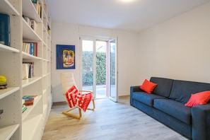 Habitación con una estantería, una silla, un sofá y un ventanal corredero que da a un espacio exterior.