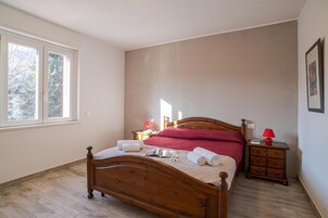 Un dormitorio con una cama de madera, una mesita de noche, una lámpara roja y una ventana con vista a árboles.