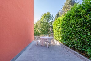 Un patio exterior con una mesa, sillas, una botella de champán y un seto.