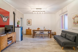 Una sala de estar moderna con un sofá, una mesa de comedor con sillas, un televisor y una cocina equipada con nevera y estufa.