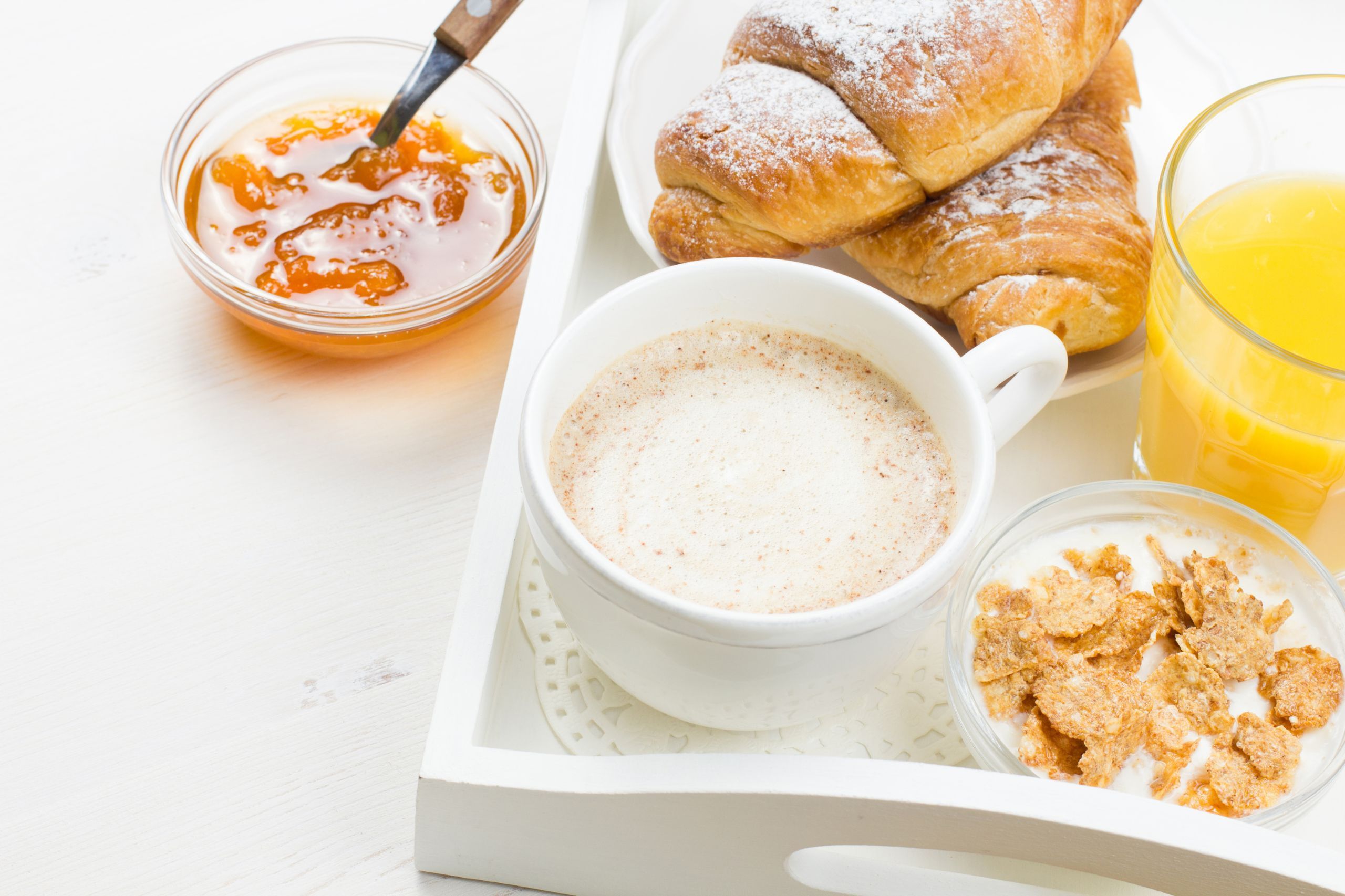 A breakfast tray with croissants, a cup of coffee, a glass of orange juice, and a bowl of cereal with fruit pieces.
