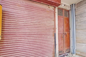 A closed red shutter door with a metal latch and a small window with a lattice design. - Hotel O Krishna Residency (Noida)
