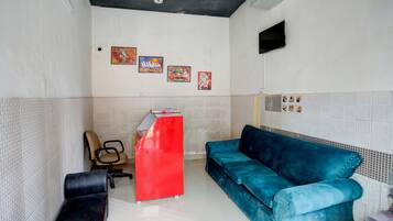 Una habitación con un escritorio rojo, un sofá azul, una silla de oficina negra y un televisor montado en la pared.