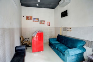 Une pièce avec un bureau rouge, un canapé bleu, un fauteuil de bureau noir et un téléviseur fixé au mur.
