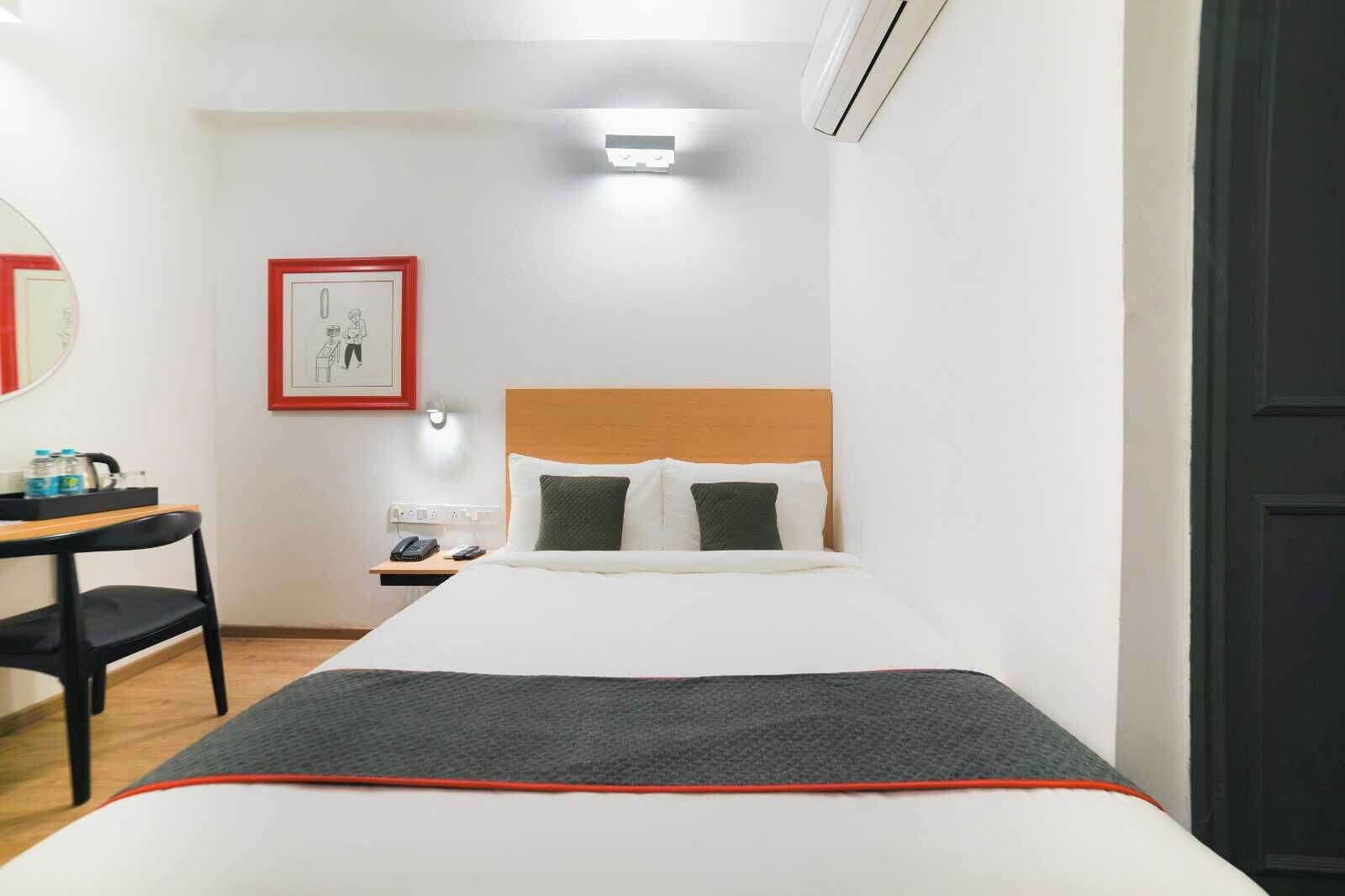 A hotel room with a bed, bedside table, chair, and a framed picture on the wall.
