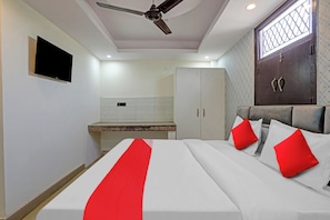 Une chambre d’hôtel équipée d’un lit, d’un ventilateur de plafond, d’une télévision, d’une armoire et d’une fenêtre avec une grille en métal.