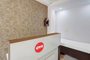Een kamer met een patroon op de muur, een witte deur en een bruin object met een rood logo.