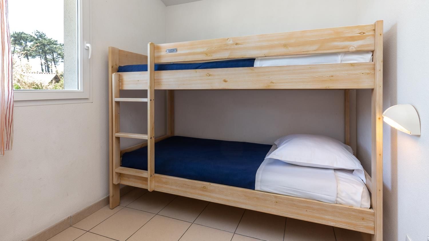Un lit superposé avec un lit inférieur et une échelle, une fenêtre avec des rideaux et une lampe de chevet.
