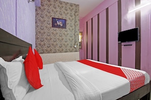 Une chambre avec un lit, un téléviseur fixé au mur et un papier peint à motifs.