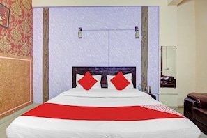 Un lit avec une couvre-lit blanche et rouge, deux oreillers rouges et une tête de lit en bois.