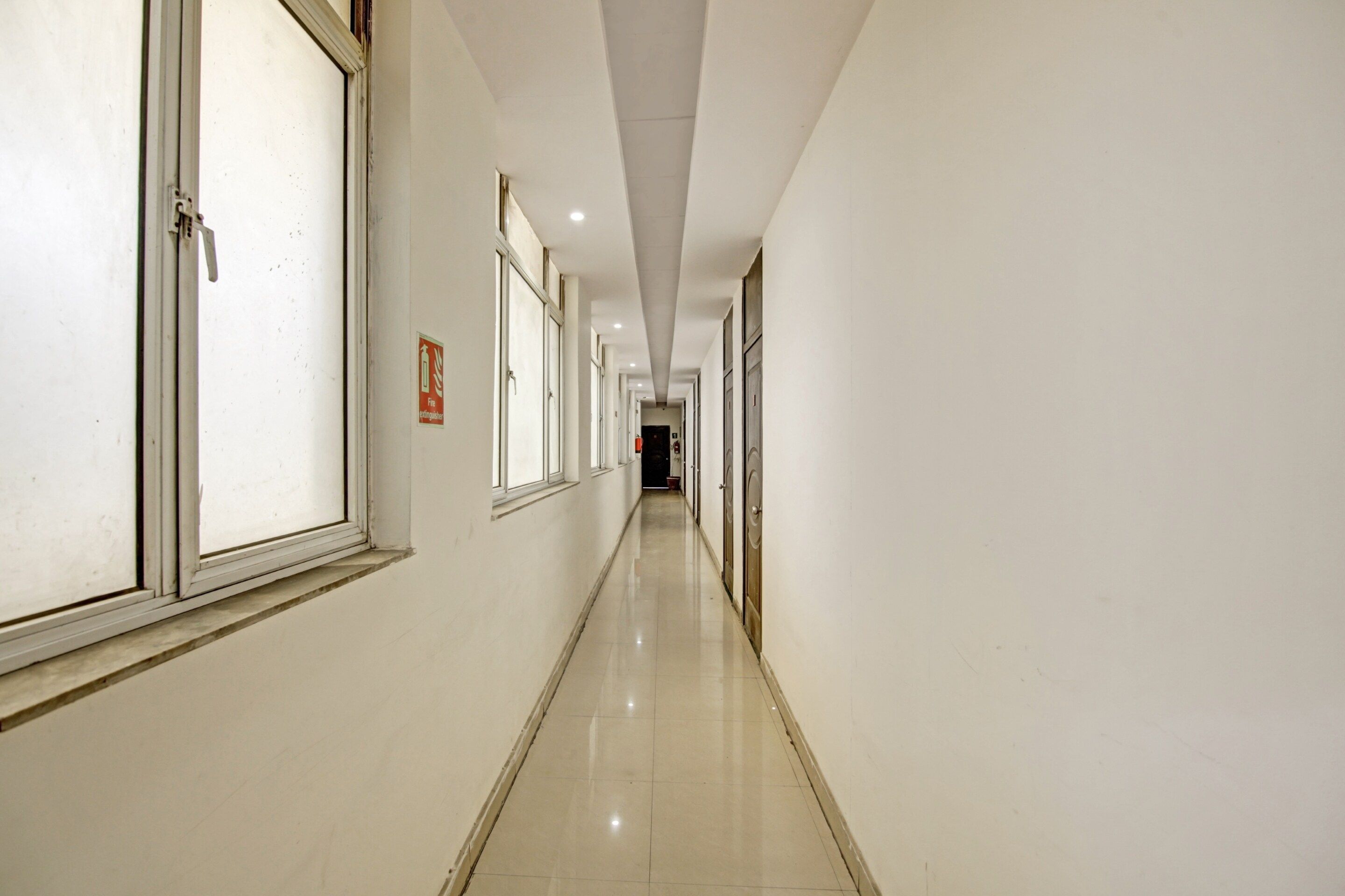 A long, narrow hallway with doors on both sides, a tiled floor, and a ceiling with recessed lighting.