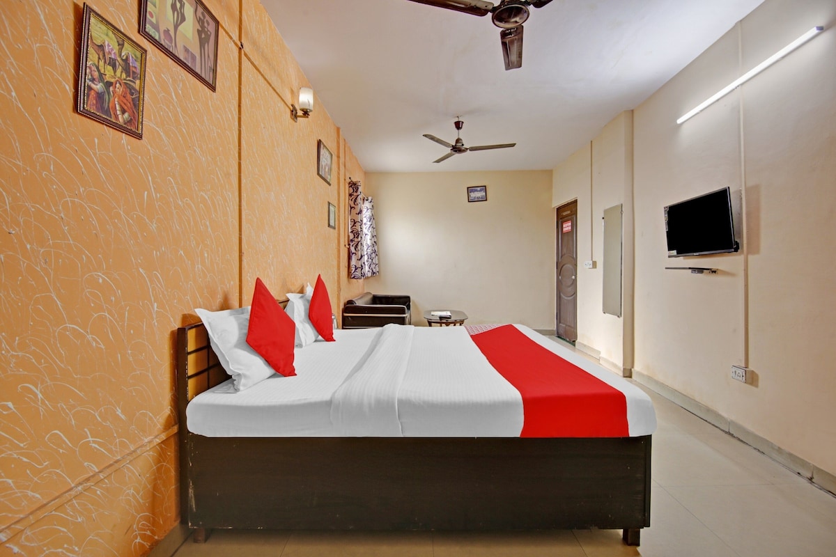 Habitación de hotel con una cama, ventilador de techo, televisor y puerta.