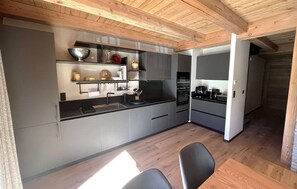 A modern kitchen with grey cabinets, a black countertop, and a wooden ceiling. - Chalet des 3 Ours 11p (Les Deux Alpes)