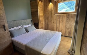 A bedroom with a bed, wooden walls, a window with a view, and a headboard. - Chalet des 3 Ours 11p (Les Deux Alpes)