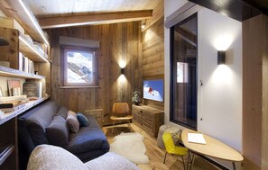 A cozy room with a wooden interior, a sofa, a chair, a small table, and a television. - Chalet des 3 Ours 11p (Les Deux Alpes)