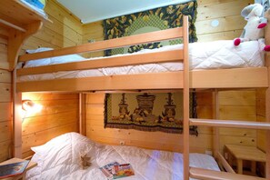 A bunk bed room with a wooden headboard, a wall tapestry, and a small table.