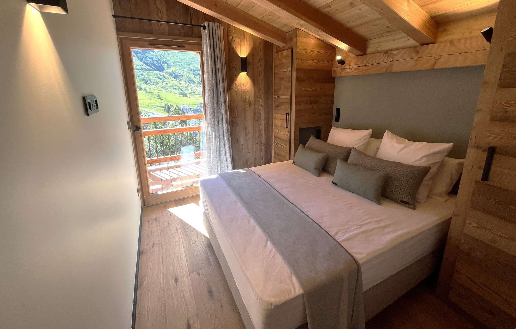 A bedroom with a bed, wooden walls, a window with curtains, and a balcony.