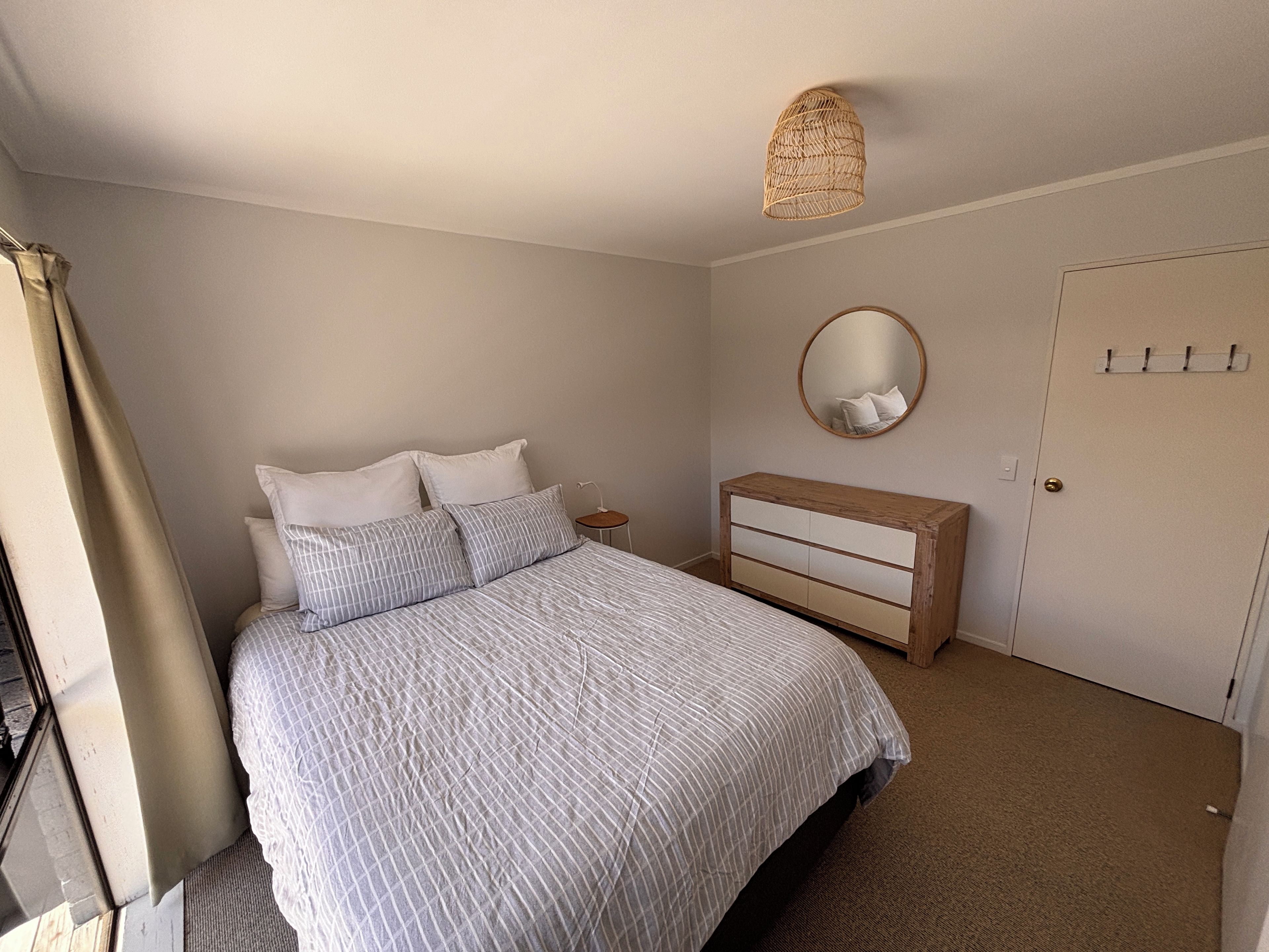 A bedroom with a bed, a bedside table, a dresser, a mirror, and a door.
