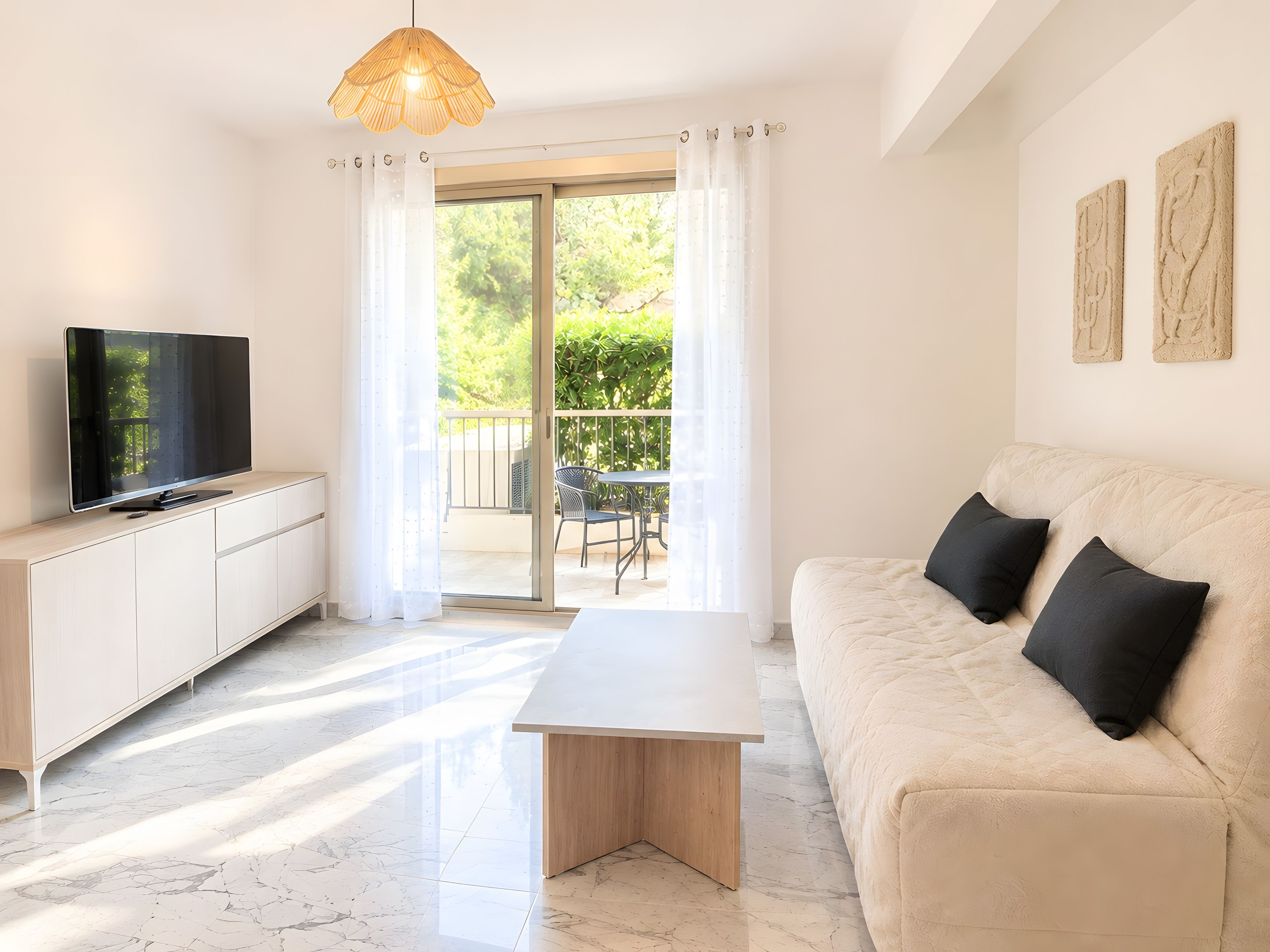 Una sala moderna con televisor de pantalla plana, un sofá con cojines negros, una mesa de centro de madera y un puerta corrediza de vidrio que da a un patio exterior.