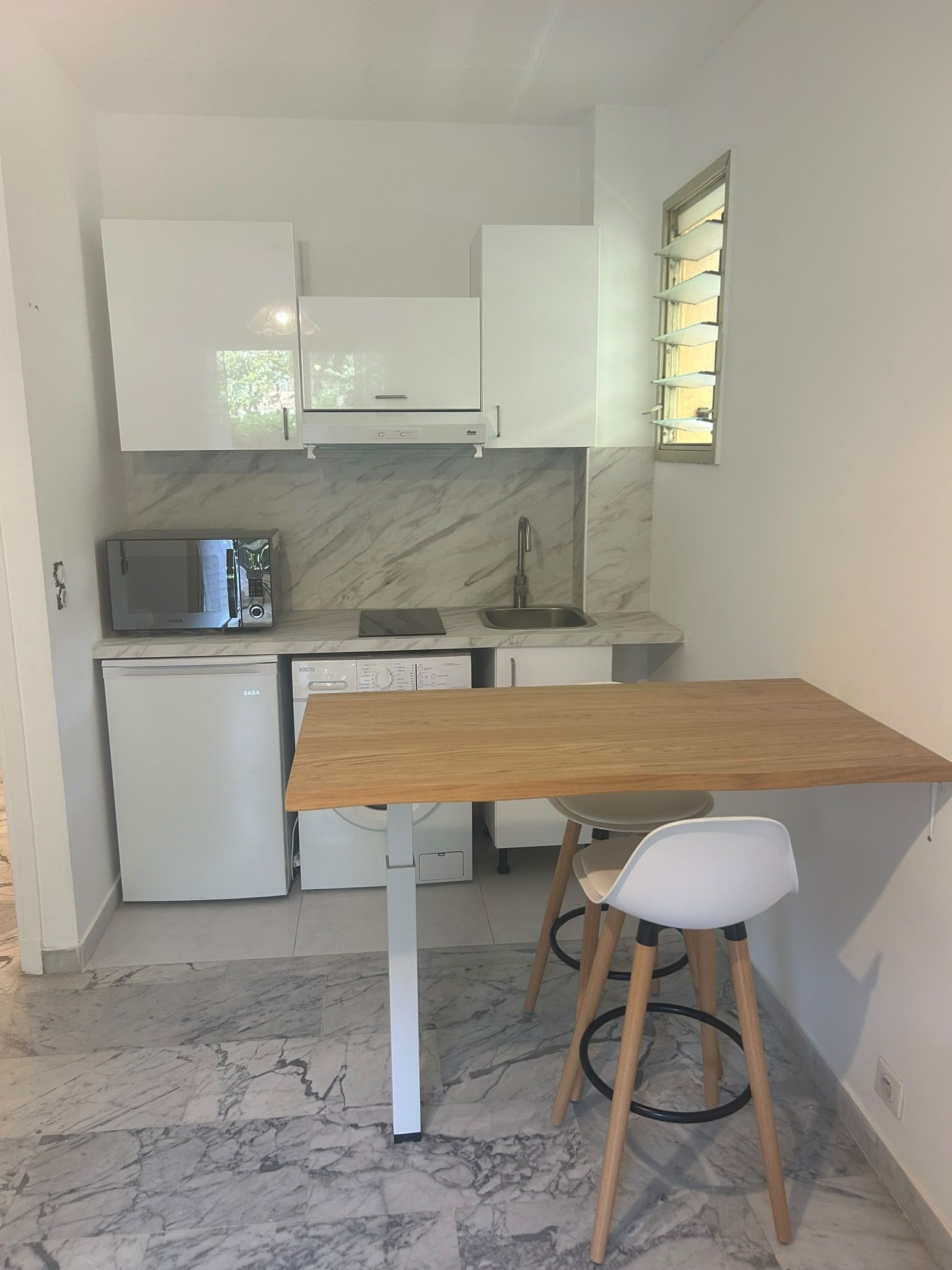 A compact kitchen with white cabinets, a microwave, a dishwasher, and a wooden table with two chairs.
