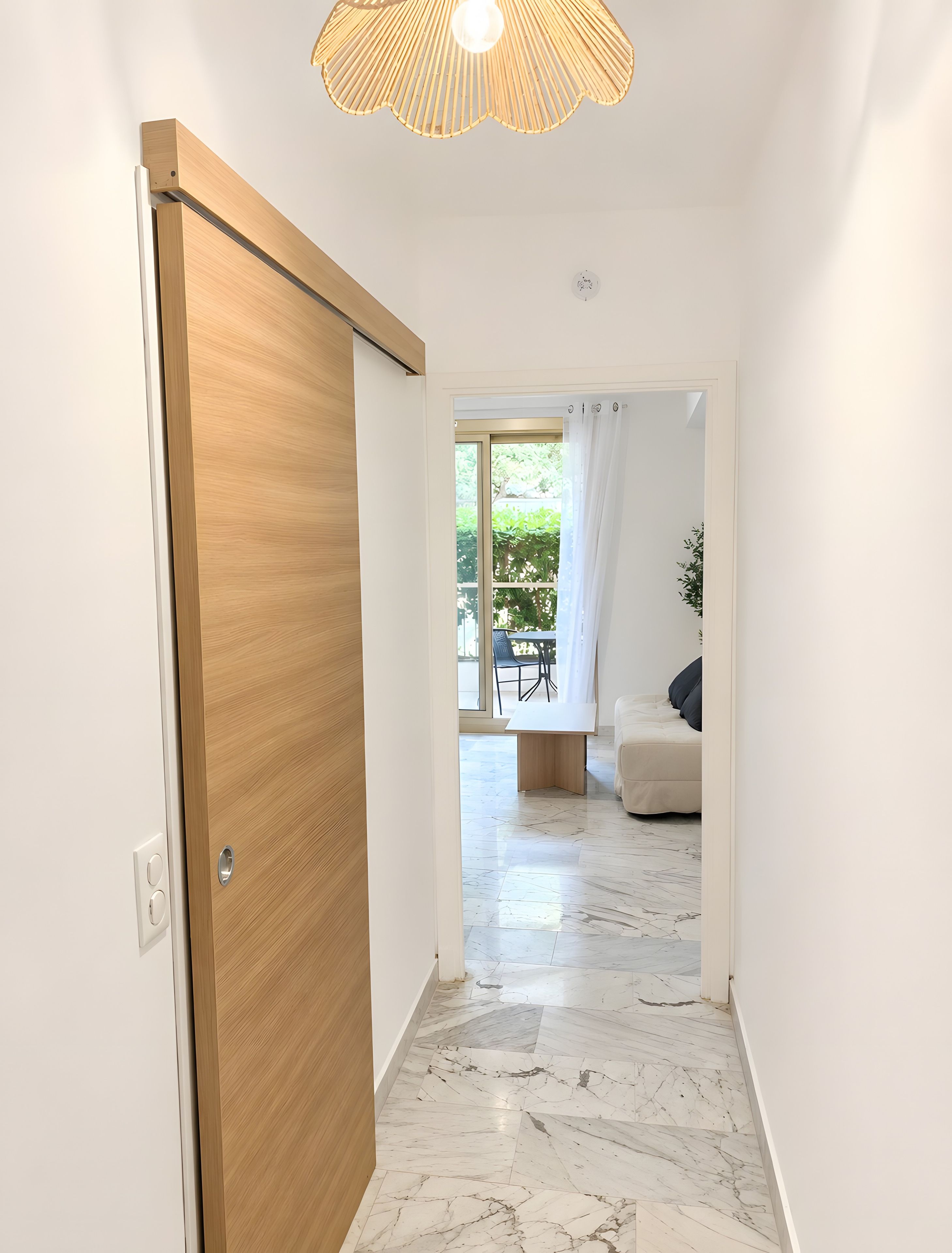 A hallway with a wooden door, a ceiling light fixture, and a view into a room with a sofa and a dining table.