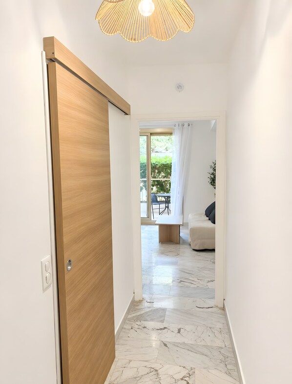 A hallway with a wooden door, a ceiling light fixture, and a view into a room with a sofa and a dining table.