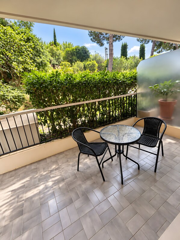 A balcony with a glass door, a round table, two chairs, and a potted plant.
