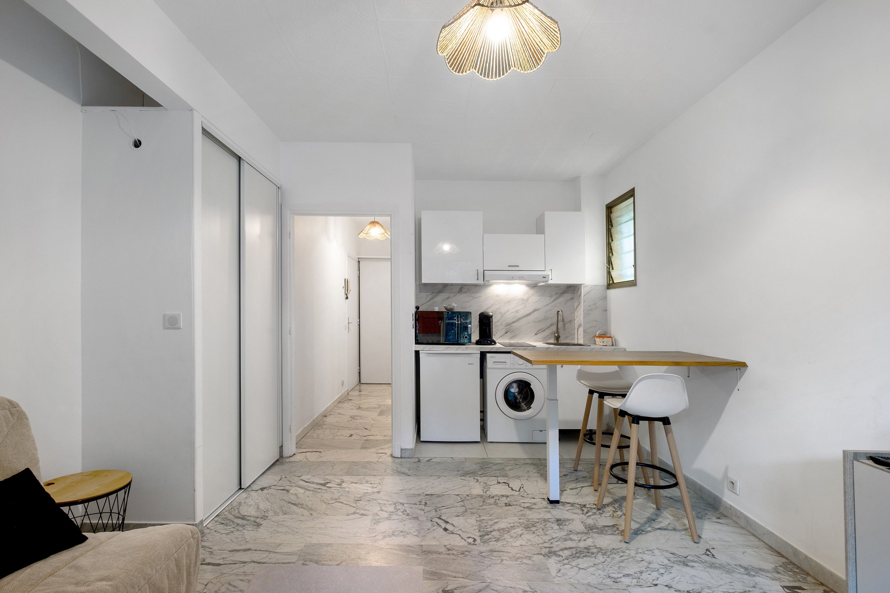 A modern kitchen with a built-in washing machine, a wooden table, and a bar stool.